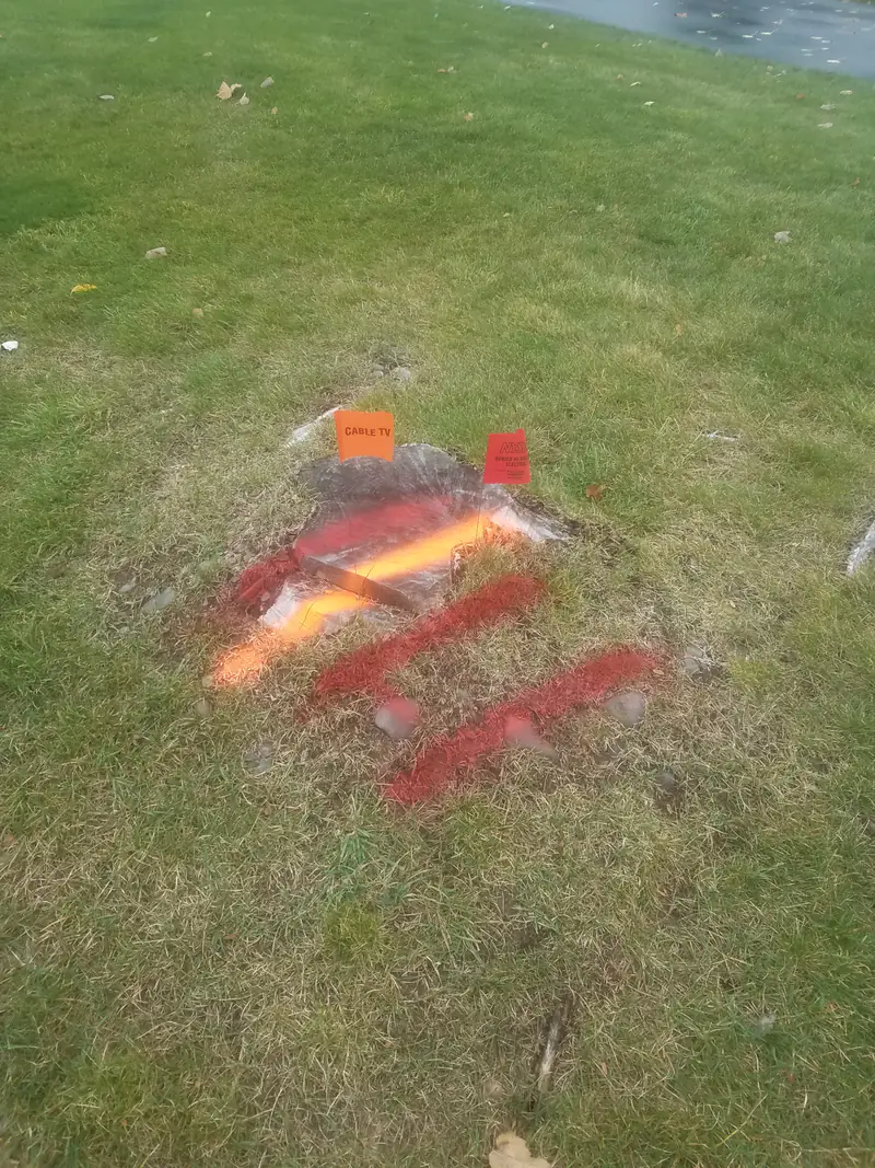Red and orange utility locate paint and small flags on a lawn